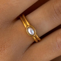 An 18K gold-plated ring with a white acrylic bead in the center, worn on a person's finger.
