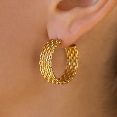 A close-up image of a woman's ear wearing a gold beaded texture hoop earring.