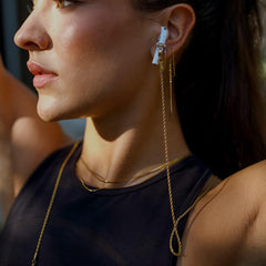 Close-up of a woman wearing gold earrings and airpods with a gold airpod chain attached with a blurred background