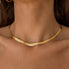 A close-up image of a person wearing a thick gold herringbone necklace.