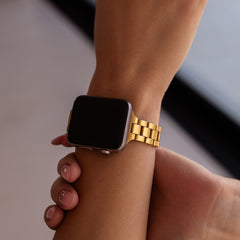 Apple Watch with a gold waterproof band on a wrist against a neutral background