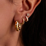 Close-up of an ear wearing gold hoop earrings with small diamond-like stones.