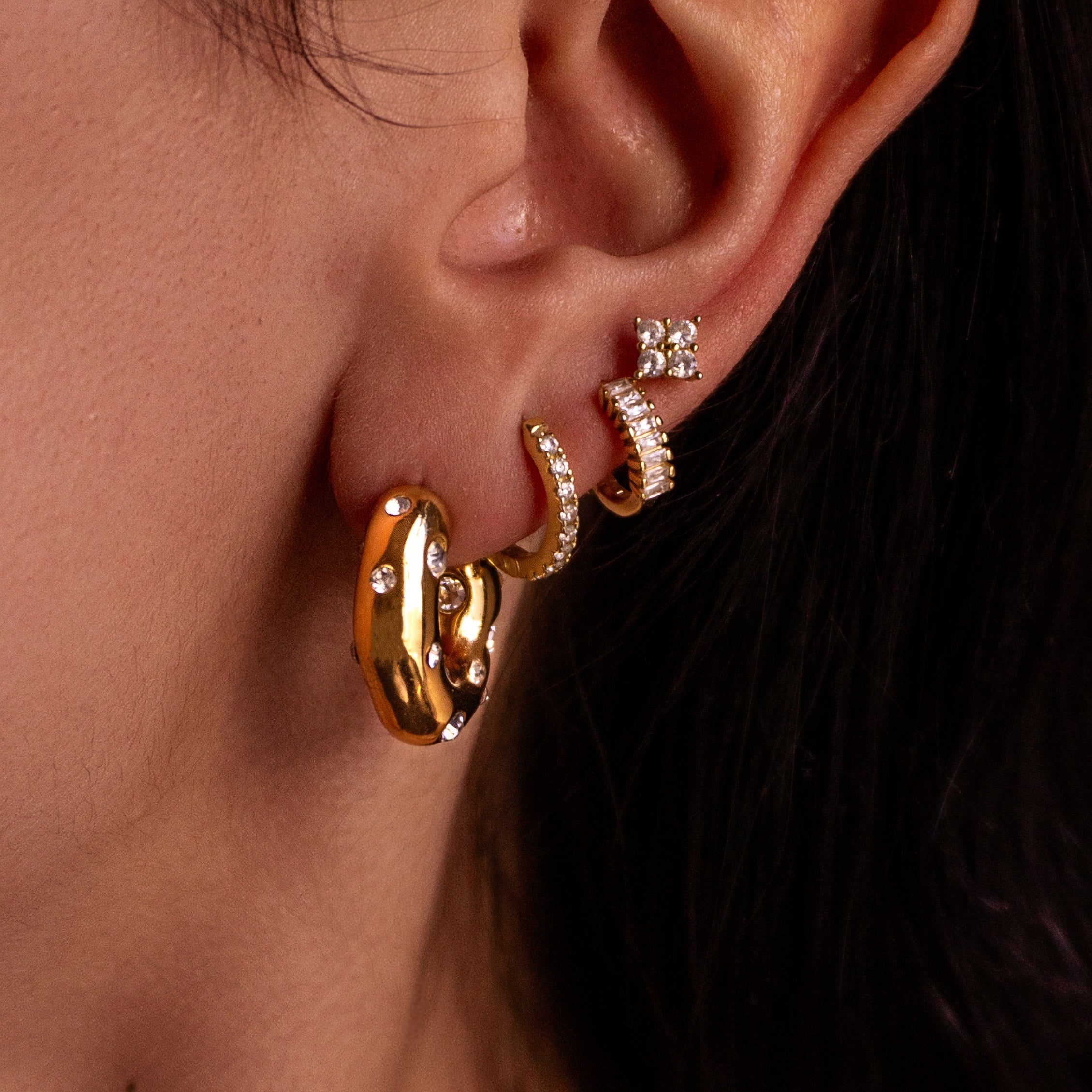 Close-up of an ear wearing gold hoop earrings with small diamond-like stones.