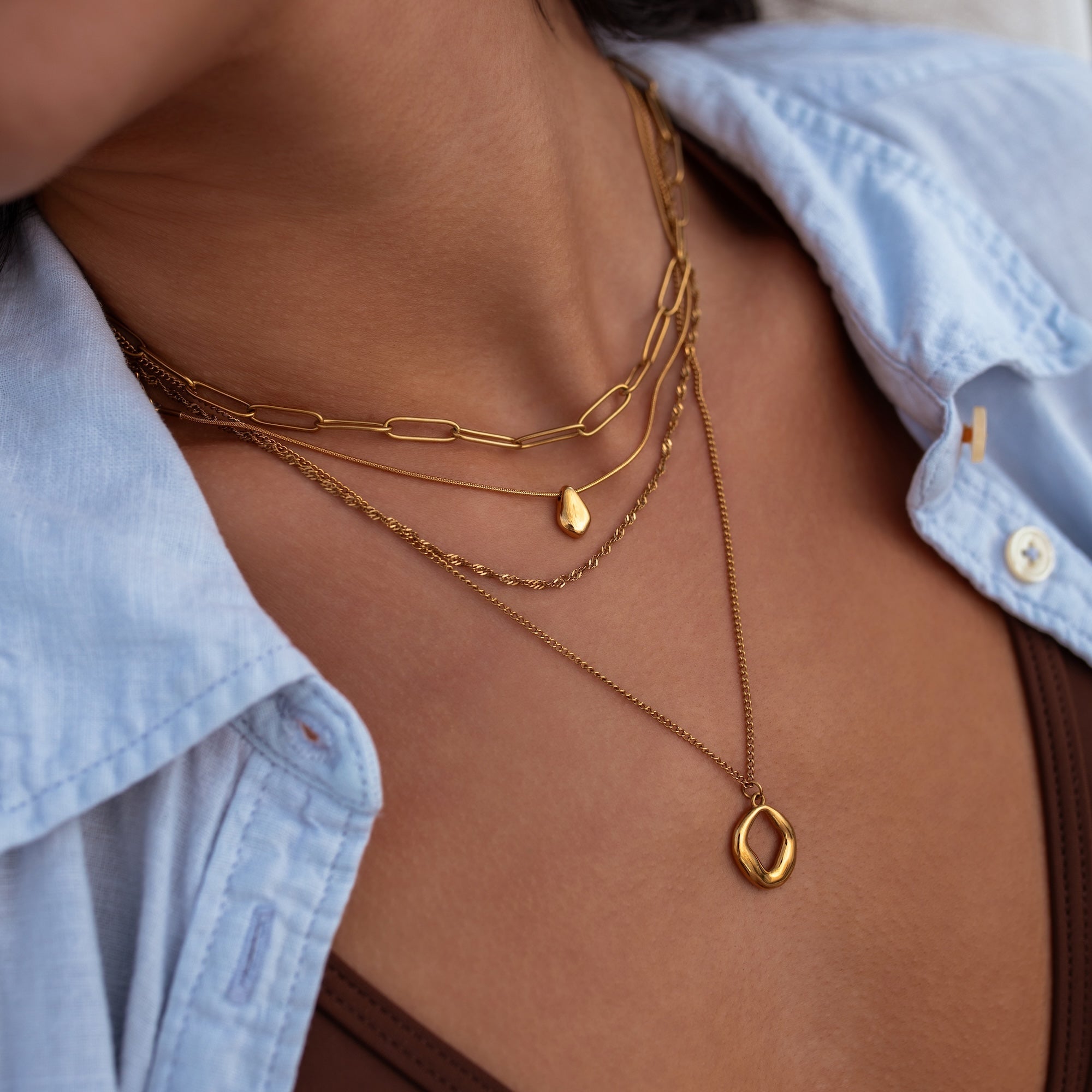 Close-up of a person wearing gold necklaces with a light blue shirt.