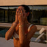 Woman in a bikini and unique gold and pearl waterproof jewelry standing under a shower with a blurred outdoor pool background