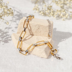 Gold and silver chain bracelet on a textured beige surface with light background